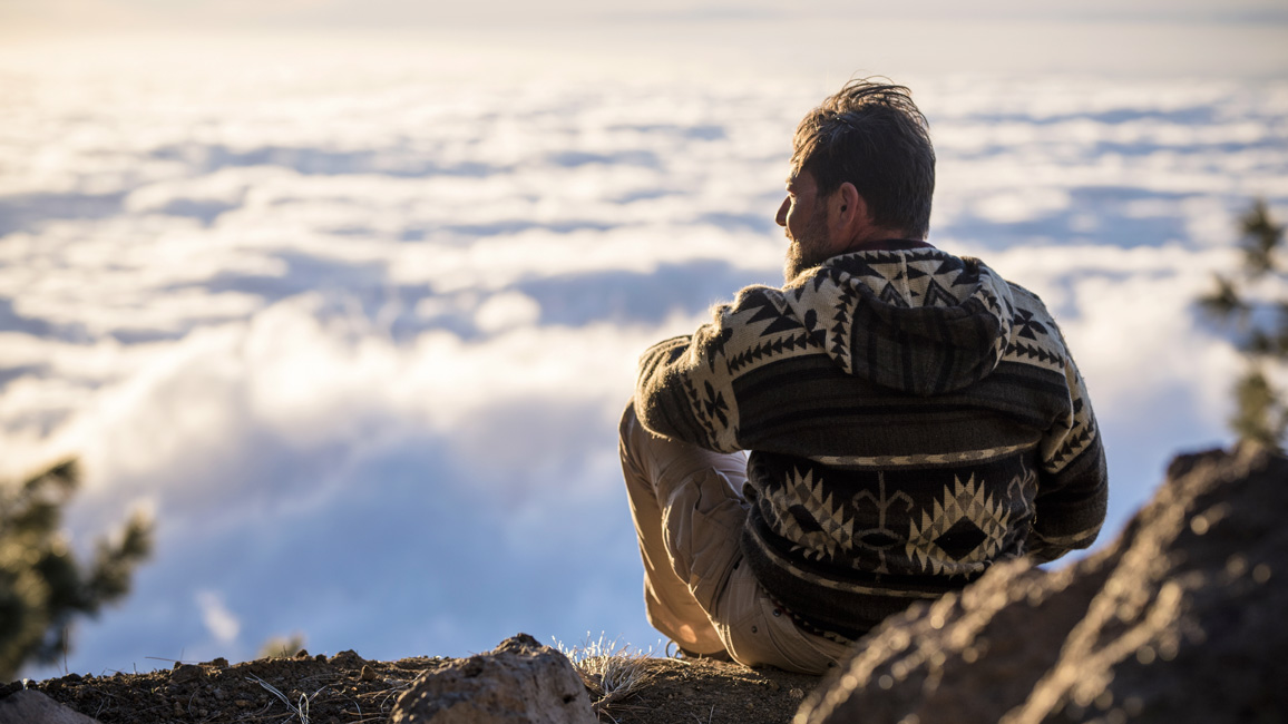 Ein Mann sitzt auf dem Gipfel eines Berges und blickt in die Ferne.